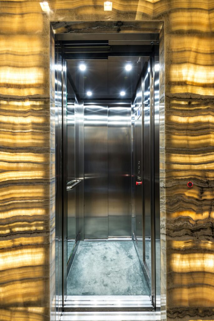 pexels-photo-7722159-7722159 Brightly lit stainless steel elevator with marble walls and modern lighting design.